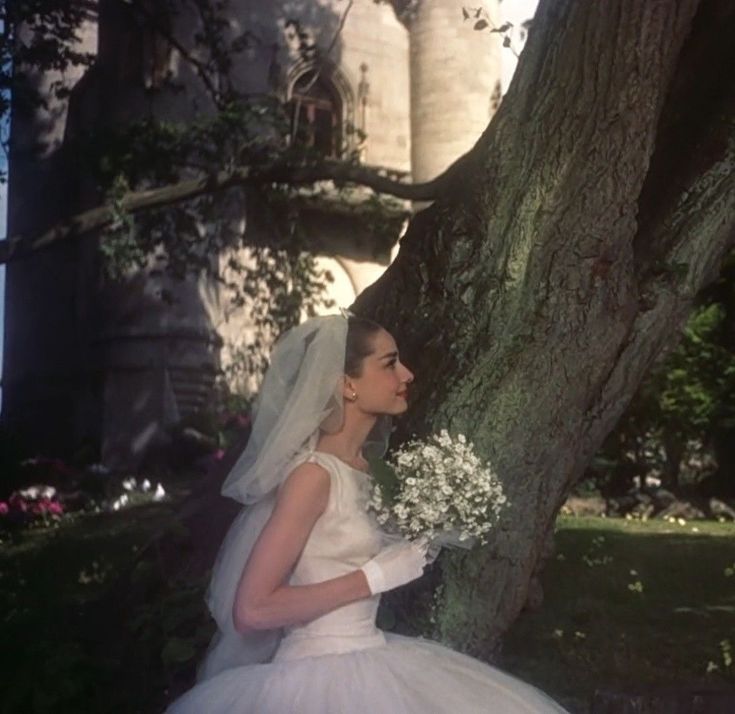 a woman in a wedding dress standing next to a tree