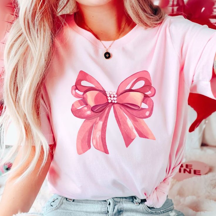 Embrace elegance and flirtatious charm with our captivating pink bow shirt, a delightful addition to your coquette-inspired wardrobe! 🌸👚 This shirt embodies the essence of femininity and playfulness, perfect for those who adore a touch of chic sophistication with a hint of flirtation. 🌷 The darling pink hue complements the shirt's design, accentuating the focal point--an exquisitely crafted oversized bow adorning the neckline or sleeves, adding a whimsical and flirtatious allure to your ensem Cute Bow T-shirt For Spring, Sweet Pink Short Sleeve Shirt, Feminine Pink Crew Neck T-shirt, Spring Party Tops With Ribbon, Feminine Party Tops With Bow Detail, Feminine Pink Summer Shirt, Feminine Pink Shirt For Summer, Cute Pink Short Sleeve Shirt, Feminine Tops With Ribbon For Spring