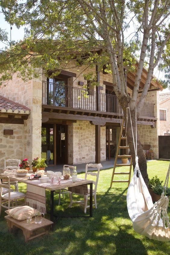 a hammock hanging from a tree in front of a house with picnic table and chairs