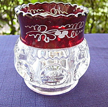 a red glass vase sitting on top of a purple table cloth next to a tree