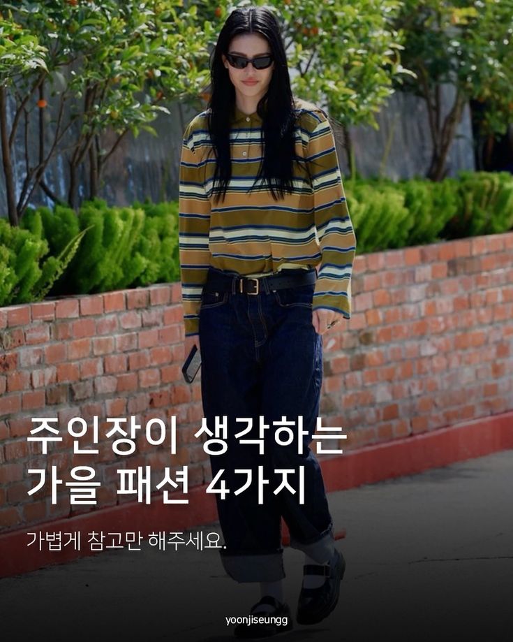 a woman standing in front of a brick wall wearing black shoes and a striped shirt