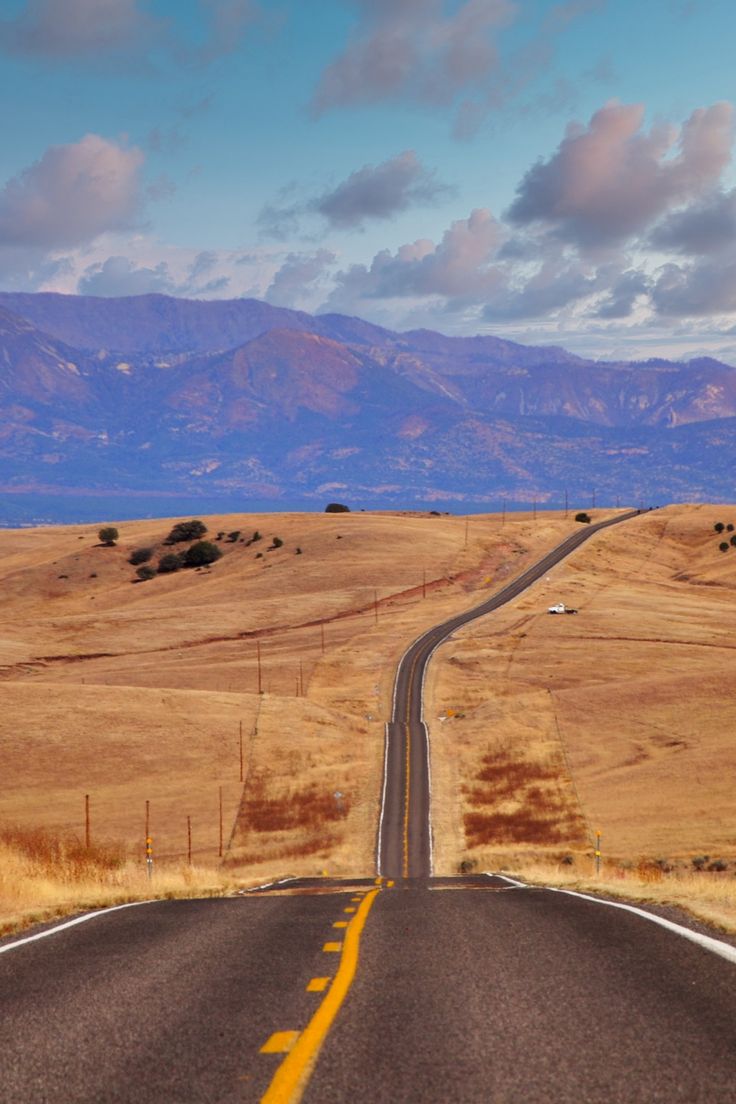 an empty road in the middle of nowhere with mountains in the background