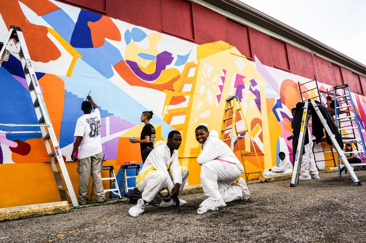 men painting a mural on the side of a building with ladders in front of them