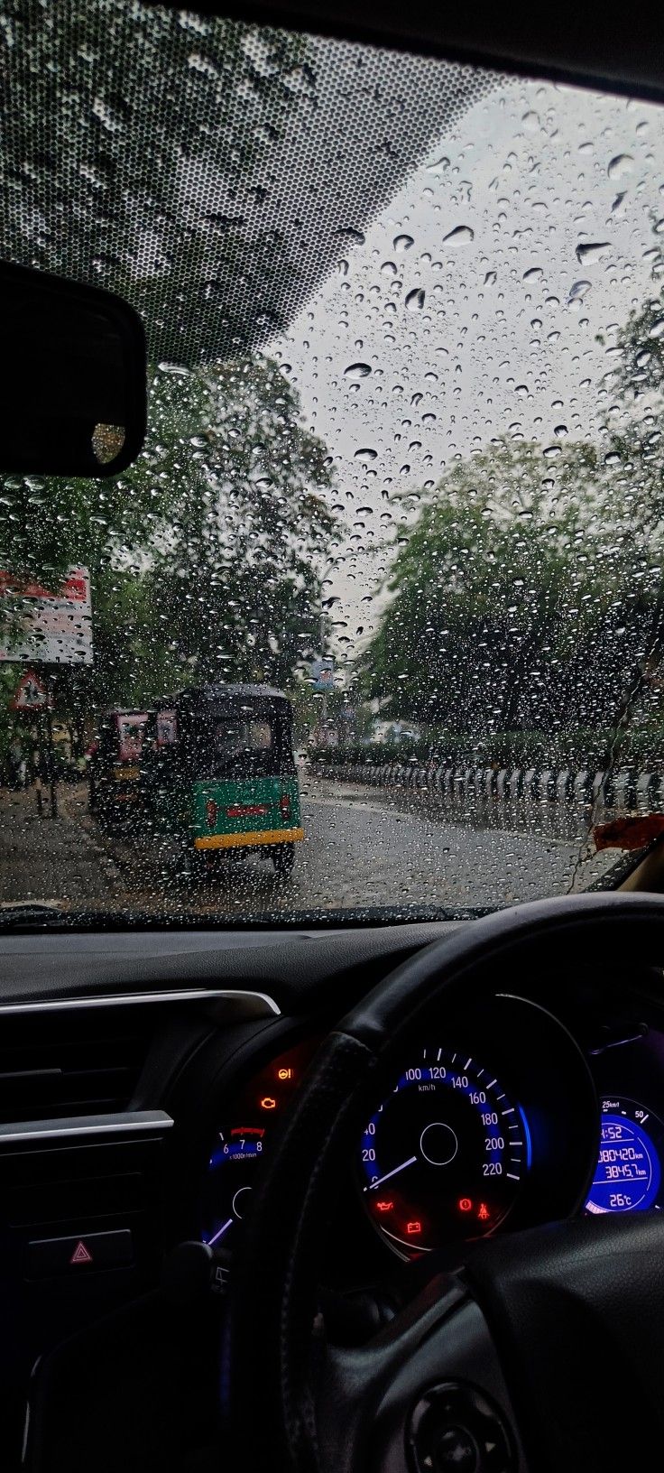 rain is falling on the windshield of a car as it drives down a street in front of a bus