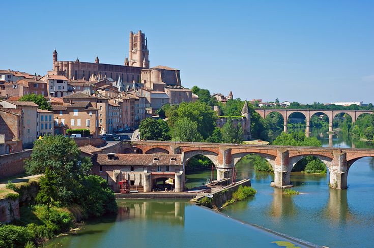 an old bridge over a river with buildings in the background and trees on both sides