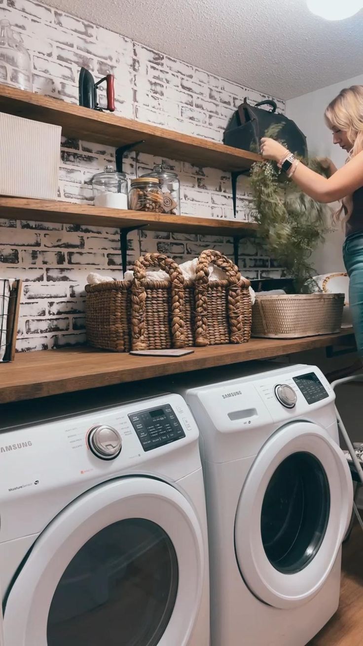 a woman standing in front of a washer and dryer next to a shelf with baskets on it