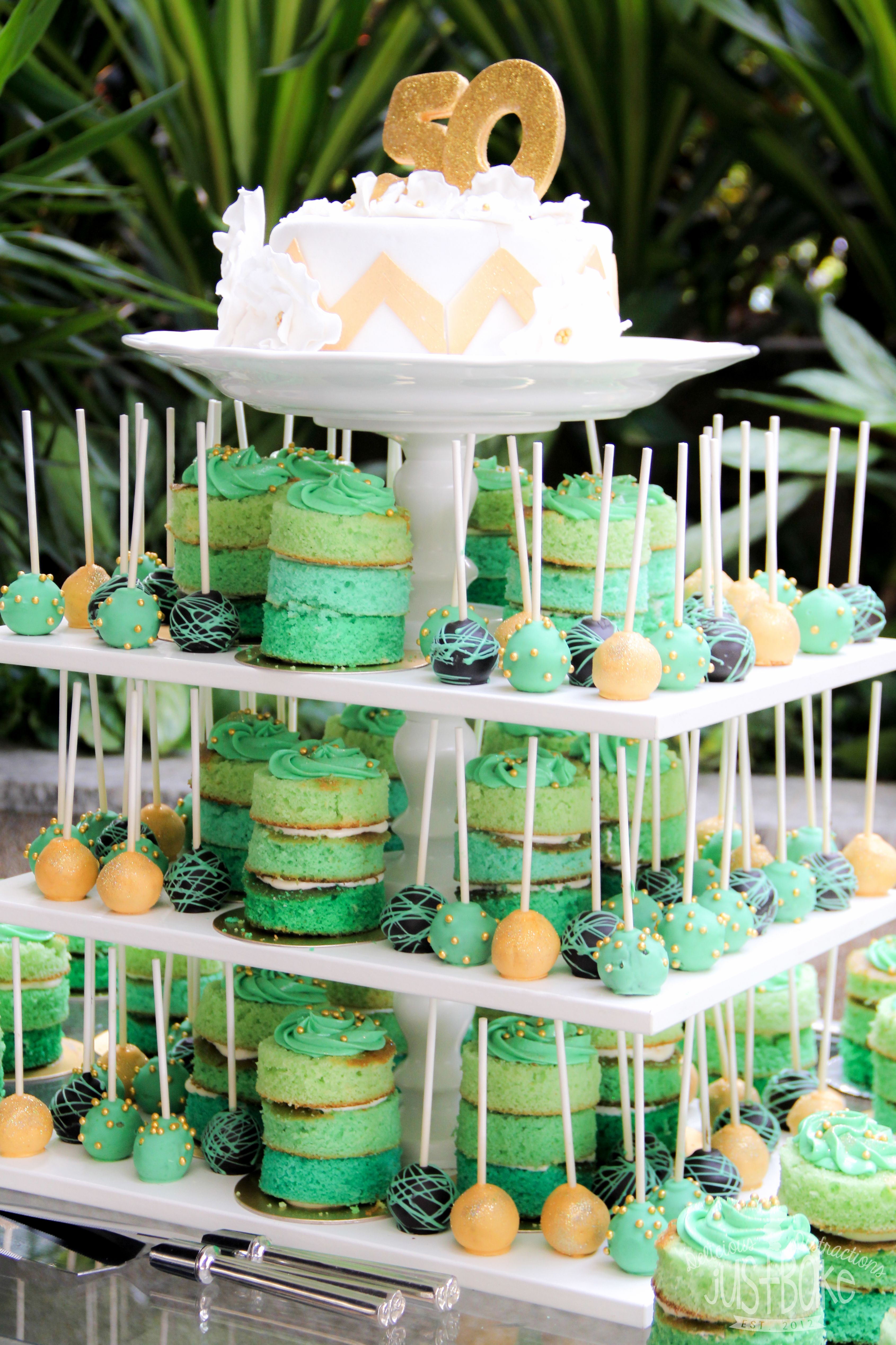 A 50th birthday party setup in a white, green and gold theme. Stands