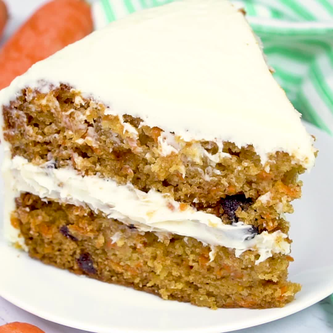 This may contain: a piece of carrot cake with white frosting on a plate next to carrots