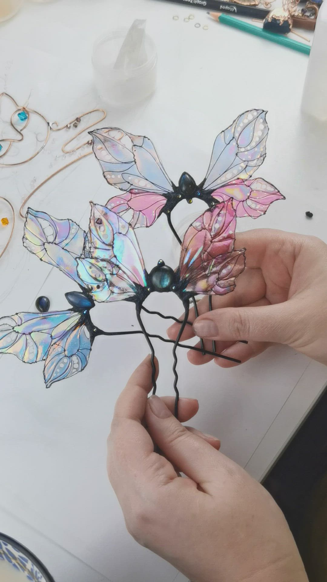 This may contain: a person is working on a wire sculpture with colored glass flowers and leaves in the shape of butterflies