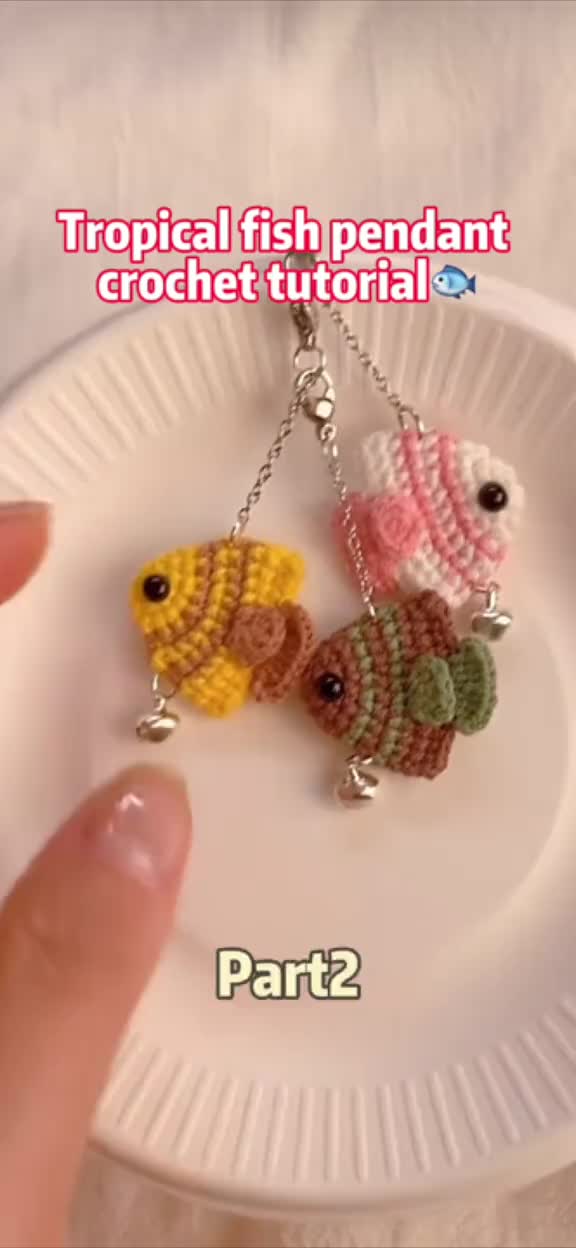 This may contain: a person is holding two tiny fish keychains on a plate with the words tropical fish pendant crochet