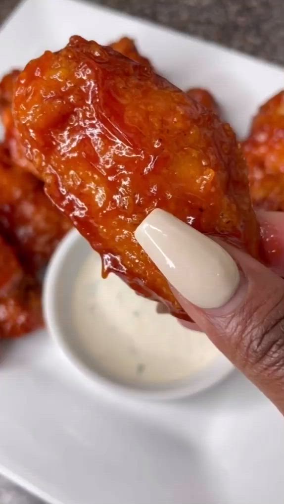 This may contain: a hand holding up a piece of chicken wings with dipping sauce on the other side