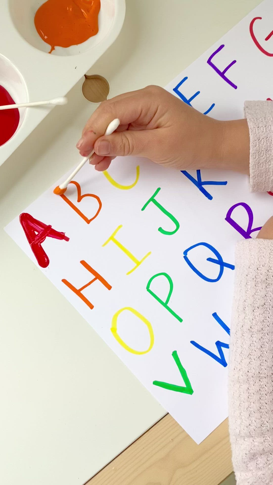 This may contain: a child's hand holding a paintbrush and painting letters on a white paper