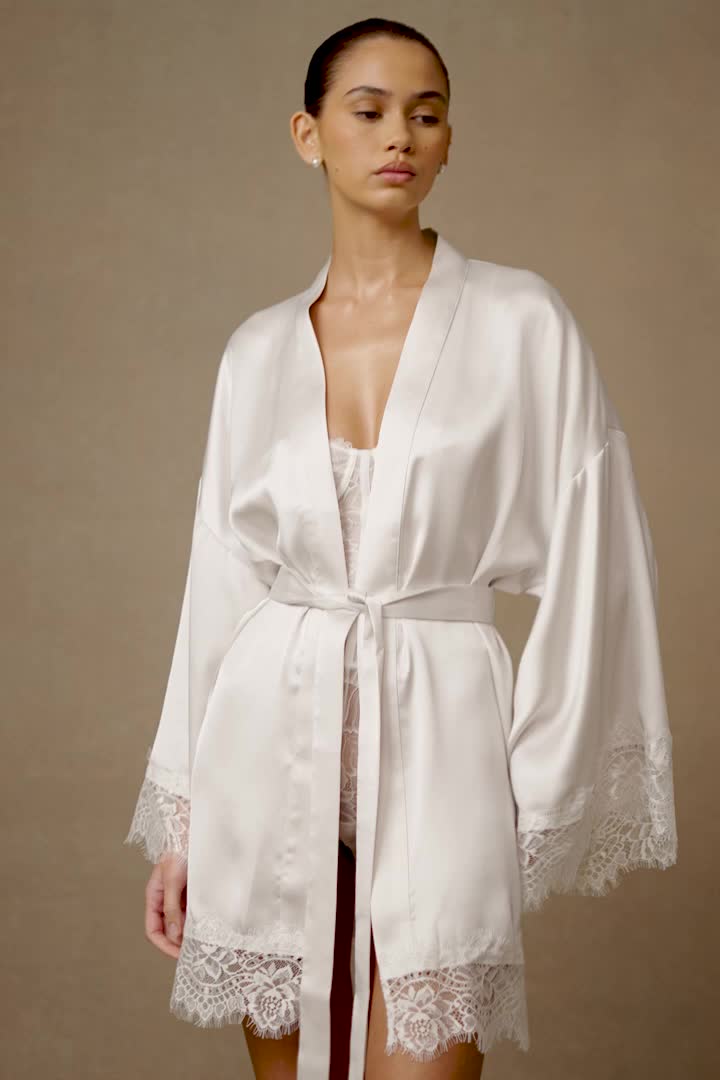 Got you covered.The ANNABETH Lace Trim Bridal Robe in White features a V neckline and wrap design, exuding elegance and sophistication. Its long sleeves and drop shoulder silhouette offer comfort and grace, while the satin fabrication adds a luxurious touch. Delicate lace trims on the sleeves and hemline add a romantic flair, complemented by the satin sash for a cinched waist. Unlined for lightweight comfort, this robe is perfect for getting ready on your special day. This style is a Pearl White