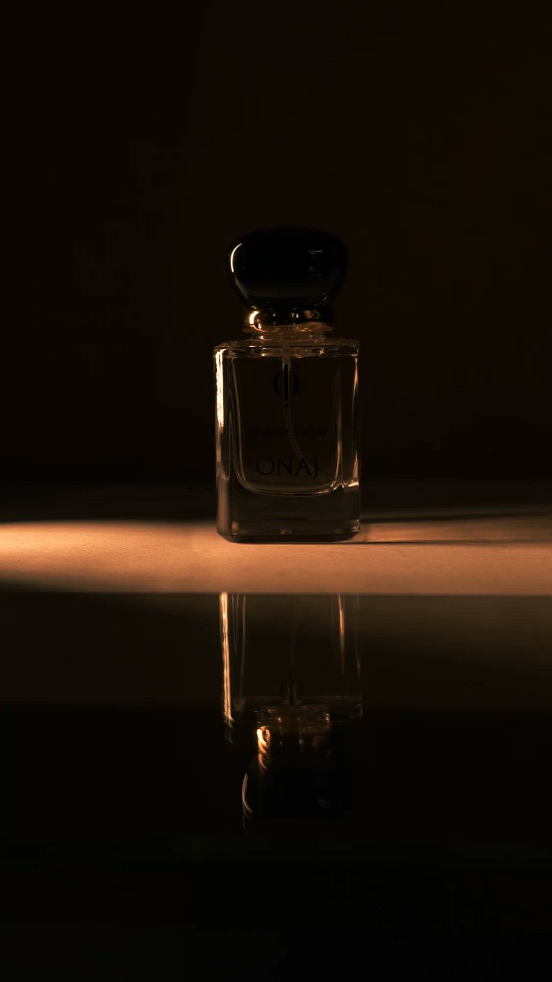 This may contain: an empty glass bottle sitting on top of a reflective surface next to a black wall