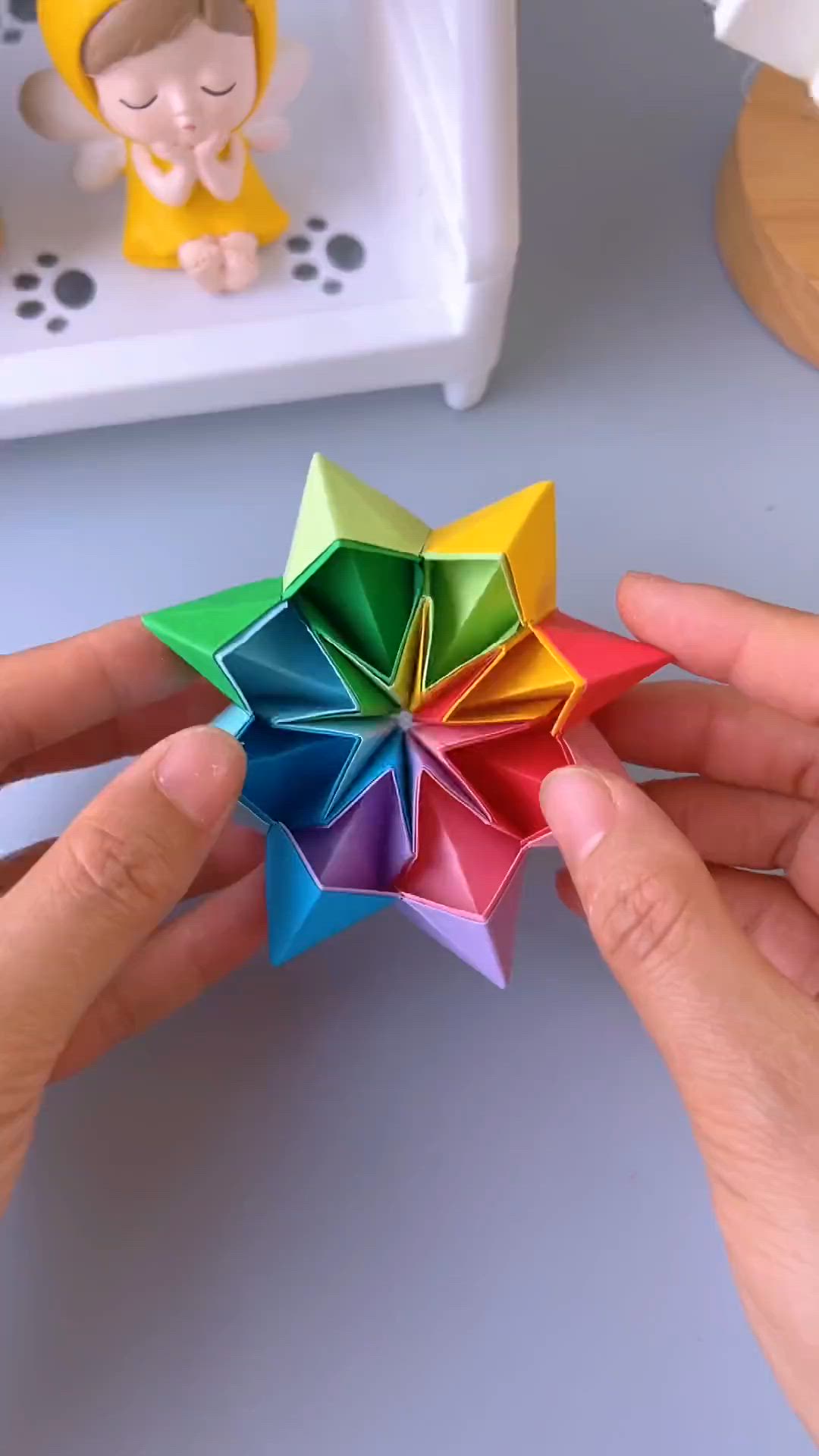 This may contain: a person is holding a colorful origami star in their left hand and another toy on the right