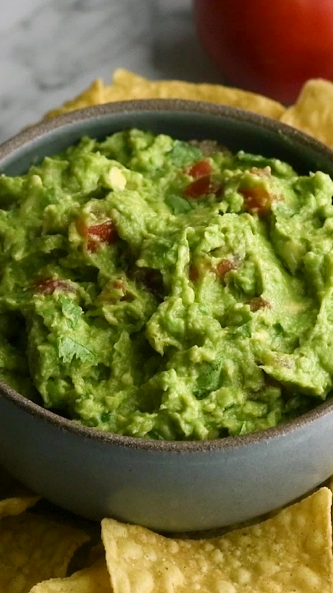 This may contain: a bowl filled with guacamole surrounded by tortilla chips and tomatoes