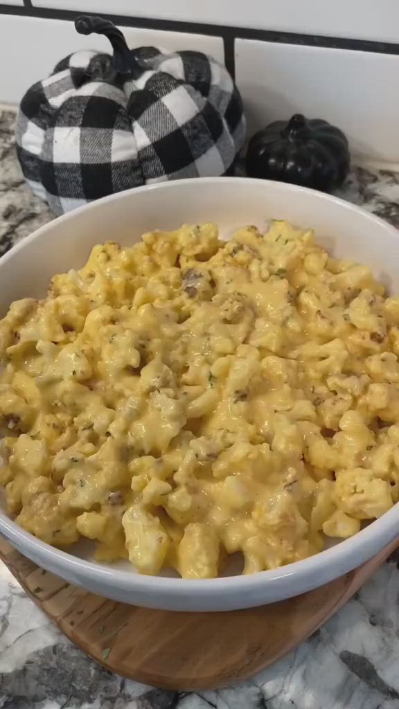 This may contain: a bowl filled with macaroni and cheese sitting on top of a counter next to a wooden spoon