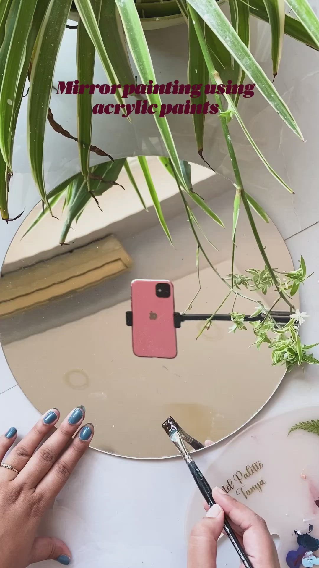 This may contain: a person painting flowers on a mirror with paintbrushes next to a potted plant