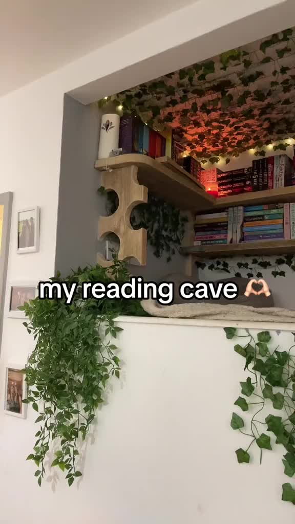 This may contain: there is a shelf with books and plants on it in front of a wall that says, my reading cave