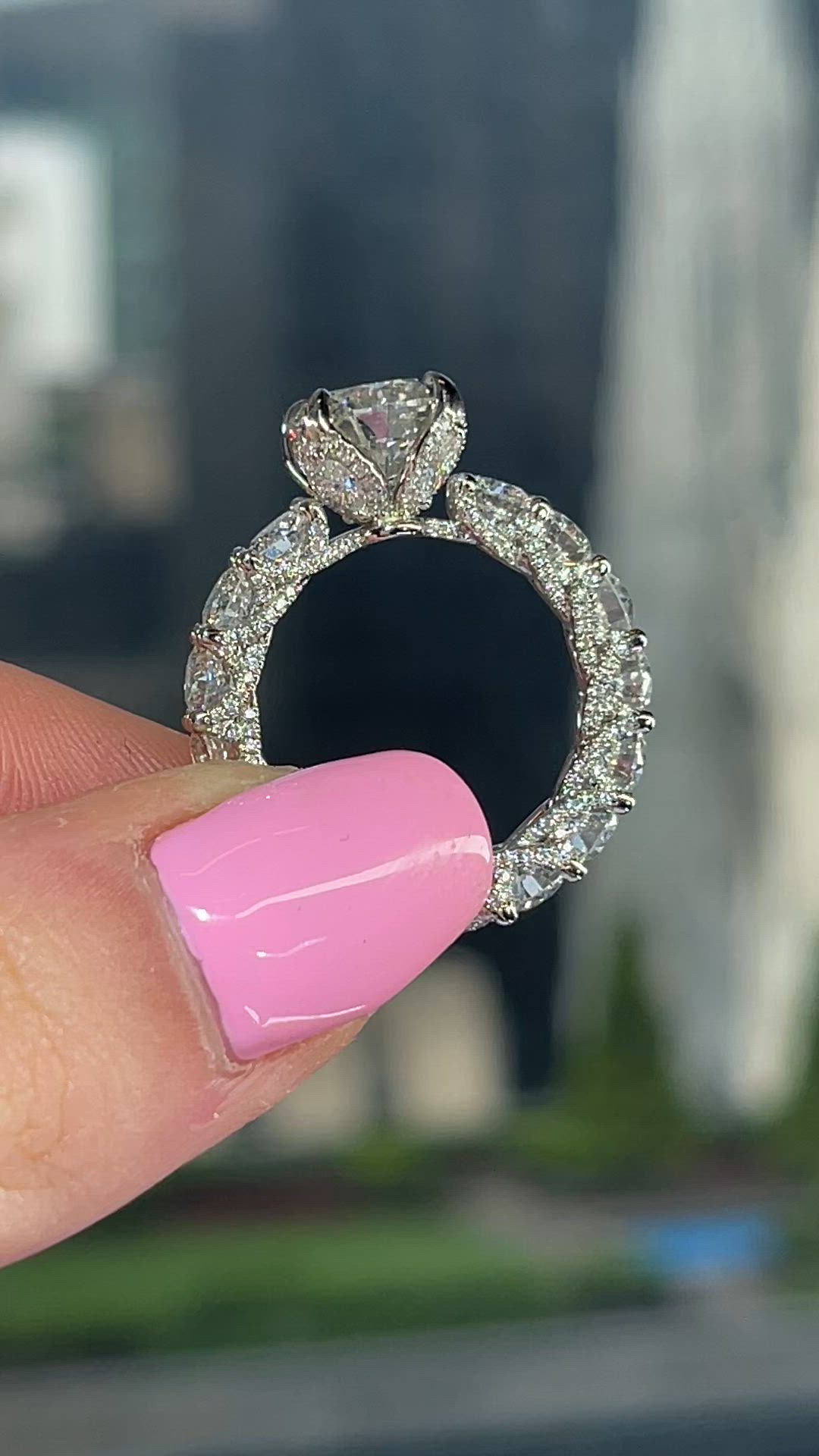 This may contain: a hand holding a diamond ring in front of a building with a pink manicure