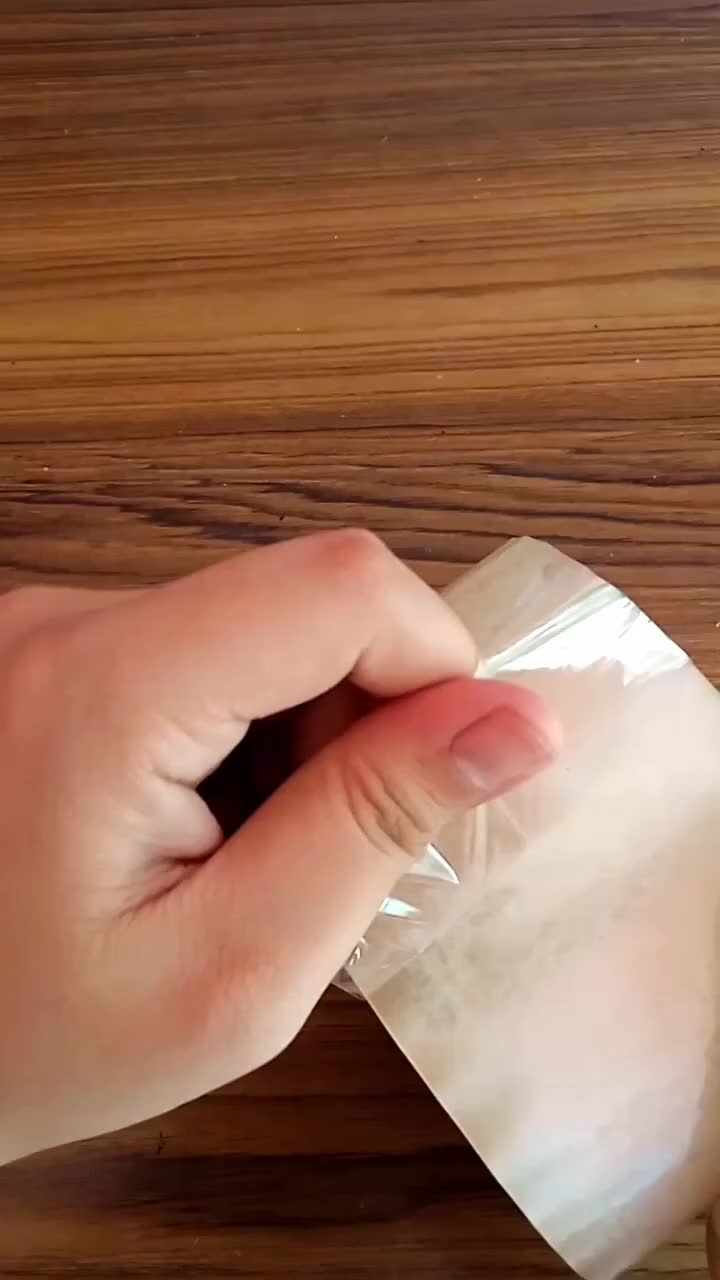 This may contain: a person's hand holding a piece of plastic wrap on top of a wooden table