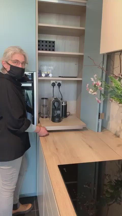 This may contain: a woman wearing a face mask standing in front of a kitchen counter with an oven and coffee maker