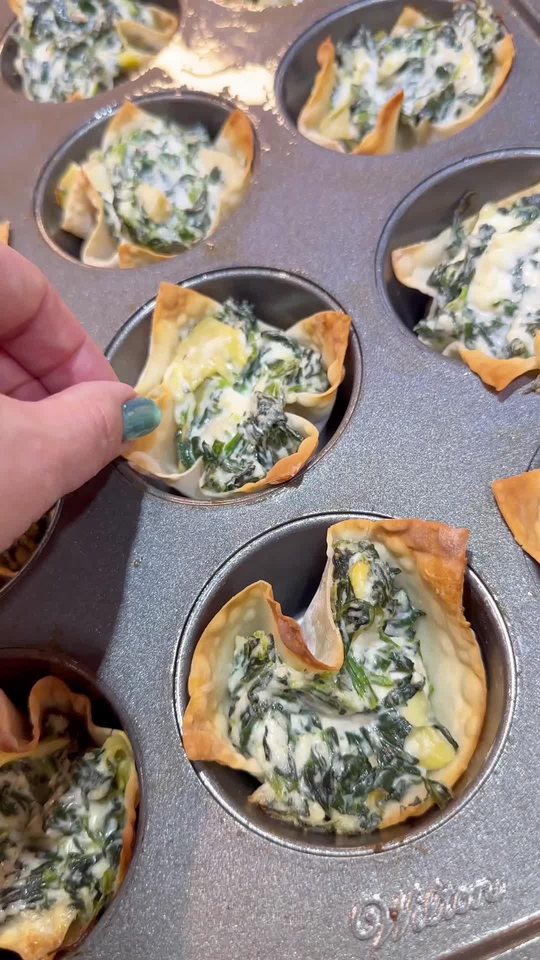 This may contain: spinach and cheese cups in a muffin tin being filled with them by a hand