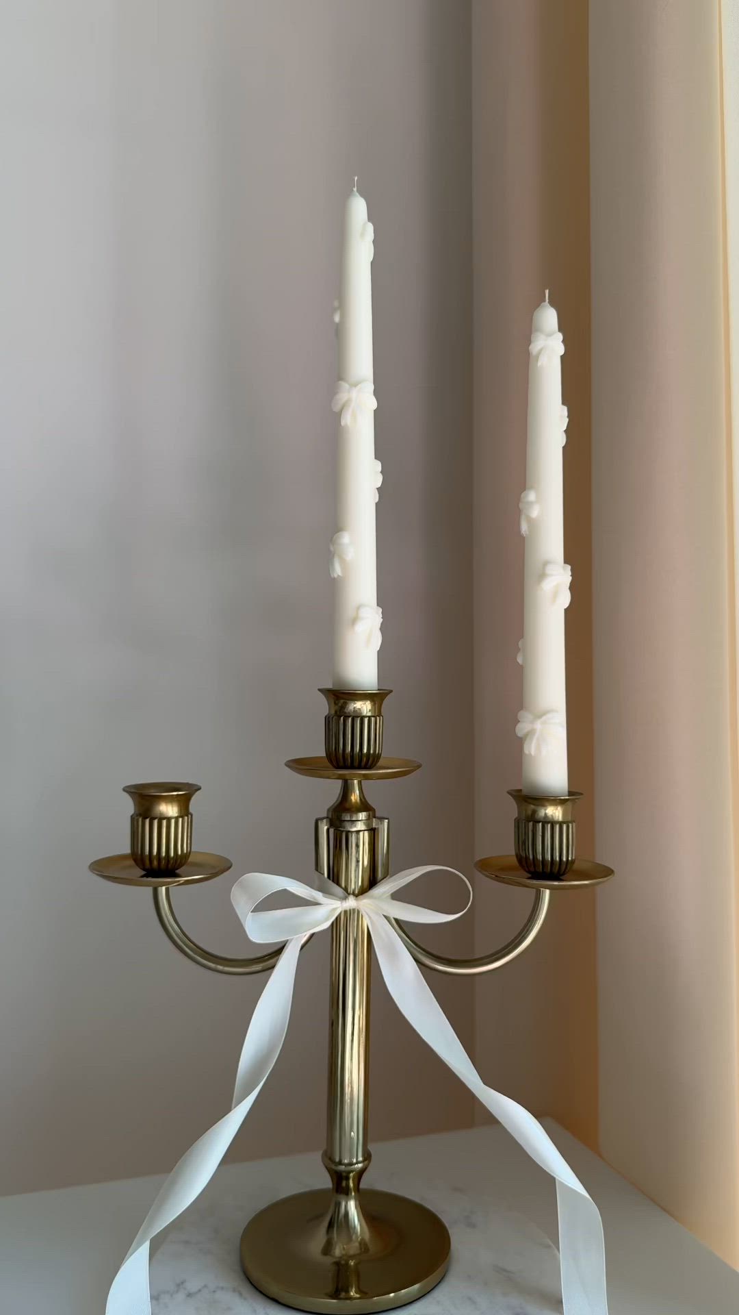 This may contain: a candle holder with three candles on it and a white ribbon tied around the top