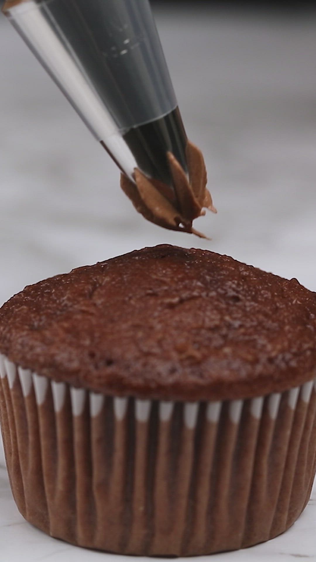 This may contain: a chocolate cupcake being dunked with icing