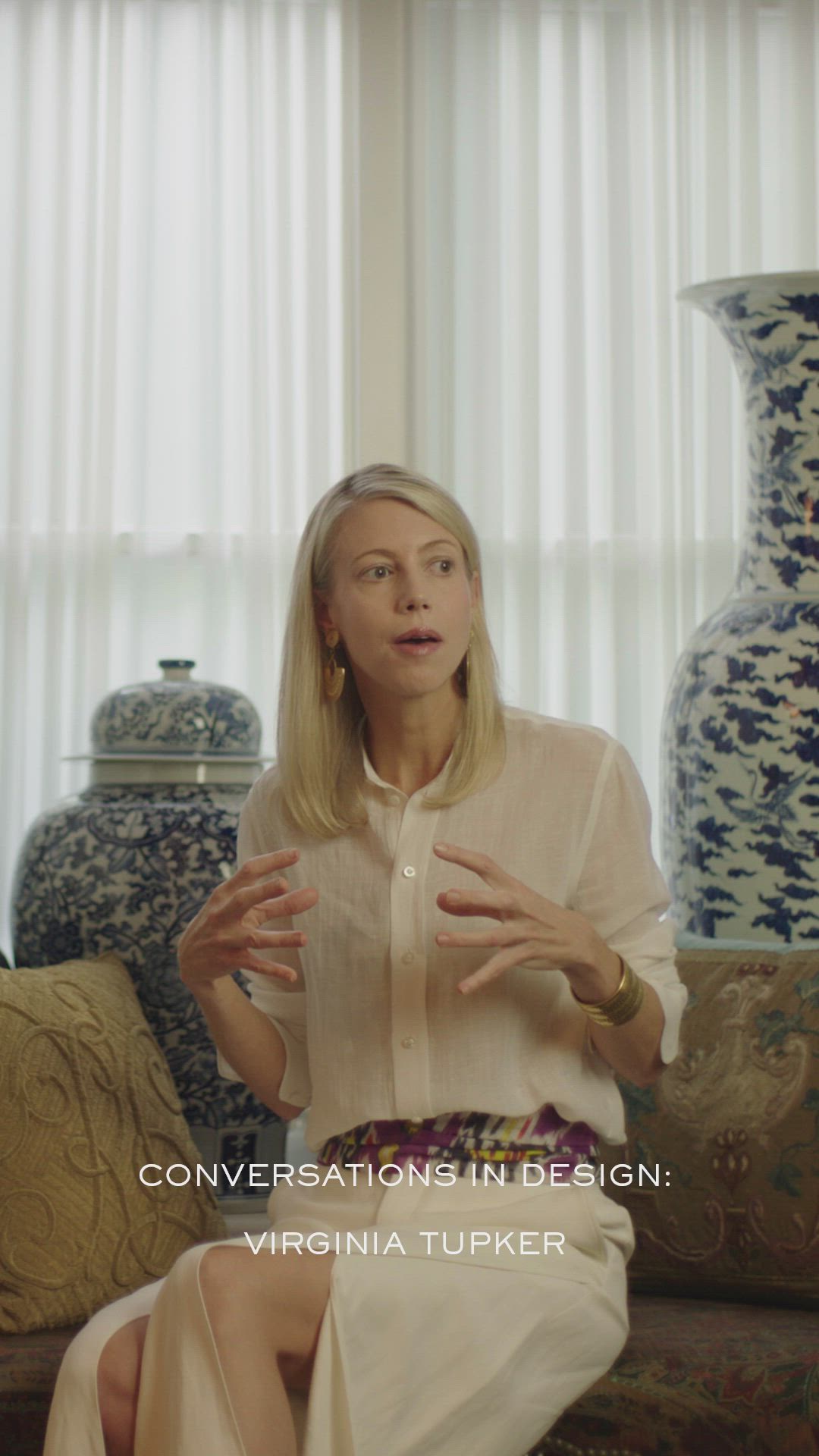 This may contain: a woman sitting on top of a couch next to vases in front of a window