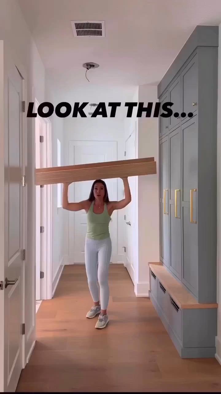 This may contain: a woman carrying a large wooden object over her head down a hallway with blue cabinets