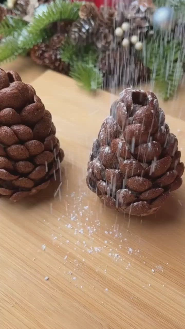 This may contain: a hand holding a small pine cone with powdered sugar on it next to two red candles