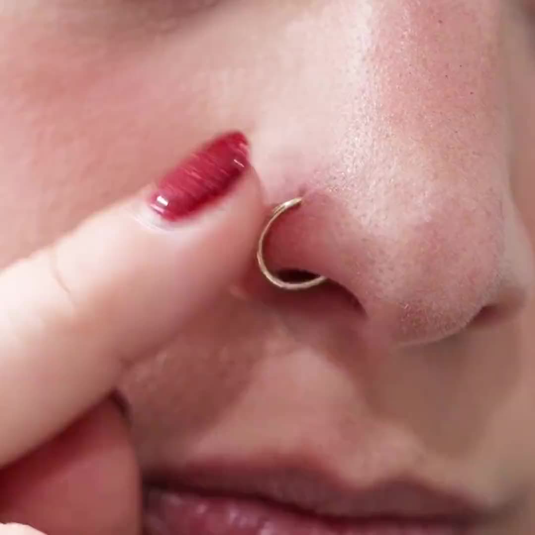 This may contain: a close up of a person with a nose ring on their nose and one finger touching the nose