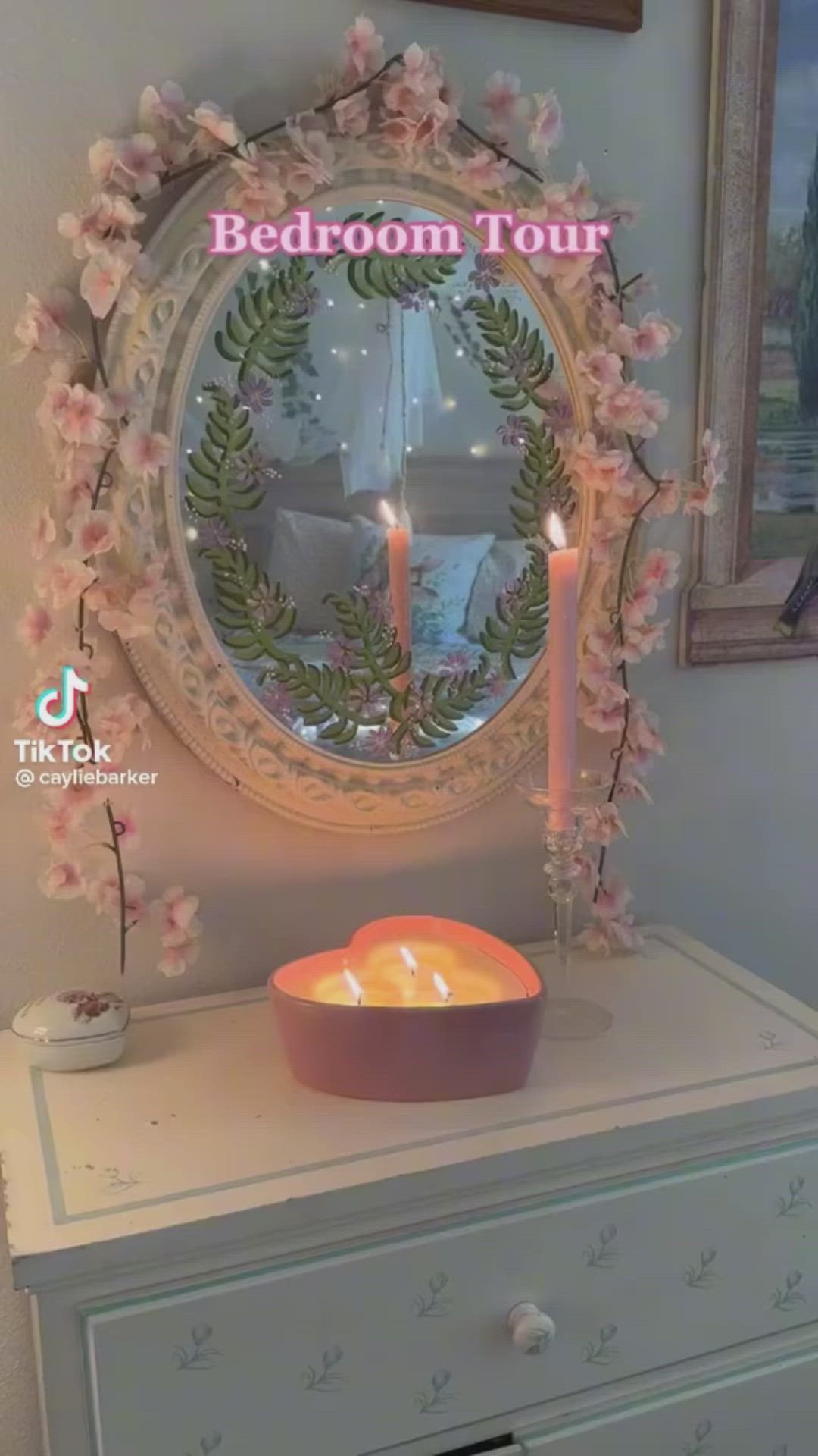 This may contain: a white dresser topped with a mirror next to a bowl filled with flowers and two lit candles