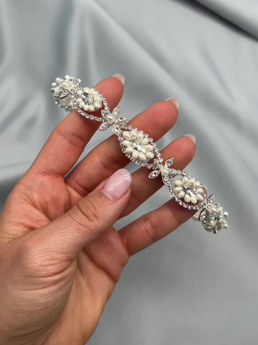 This may contain: a woman's hand holding a diamond and pearled bridal bracelet in her left hand