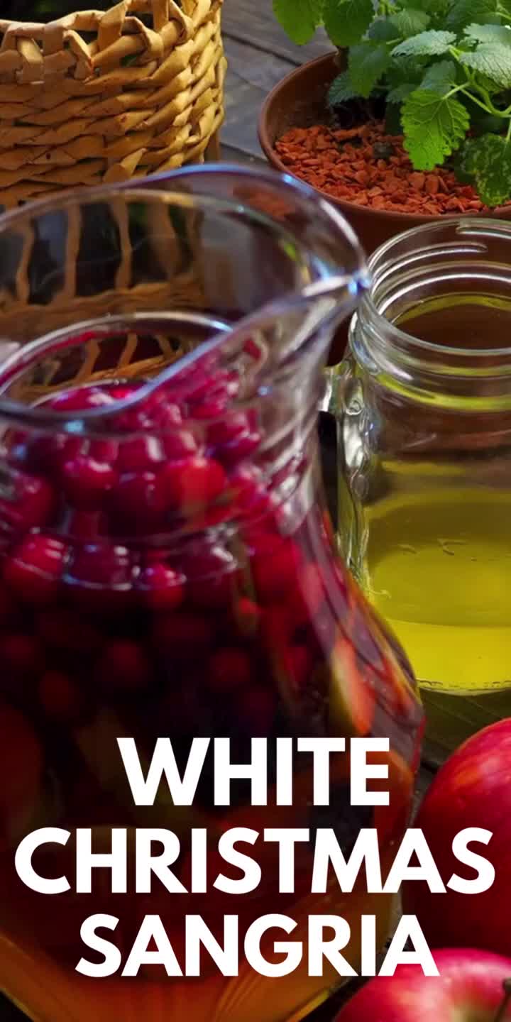 This may contain: white christmas sangria with apples and cranberries in the foreground text reads, white christmas sangria