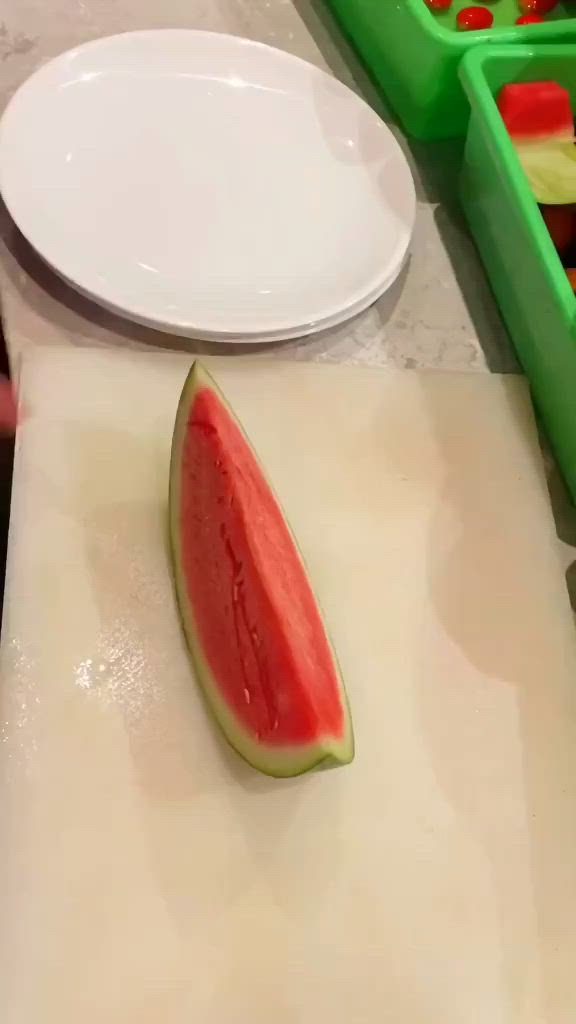 This may contain: a person cutting up fruit on top of a white counter next to green trays