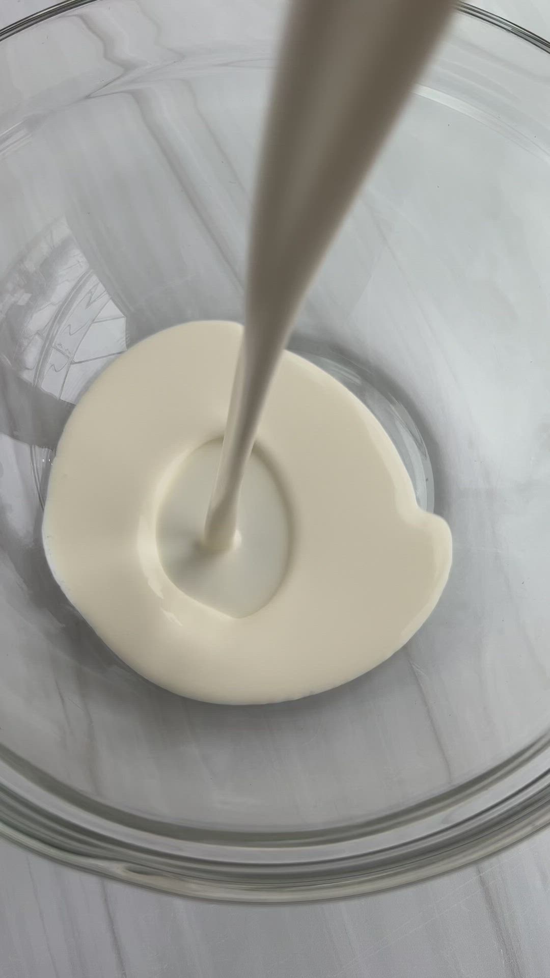 This may contain: a white bowl filled with chocolate frosting on top of a wooden cutting board