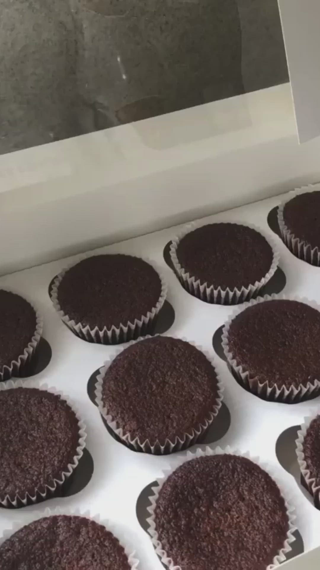 This may contain: twelve cupcakes with purple frosting in a white box on a counter top