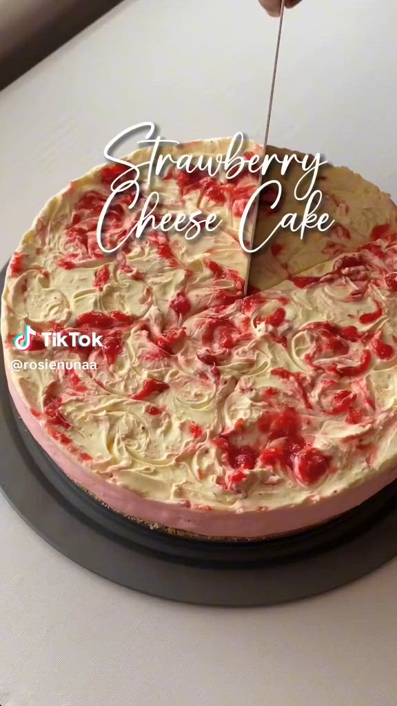 This may contain: someone cutting into a strawberry cheese cake on top of a white table with the words strawberry cheese cake above it