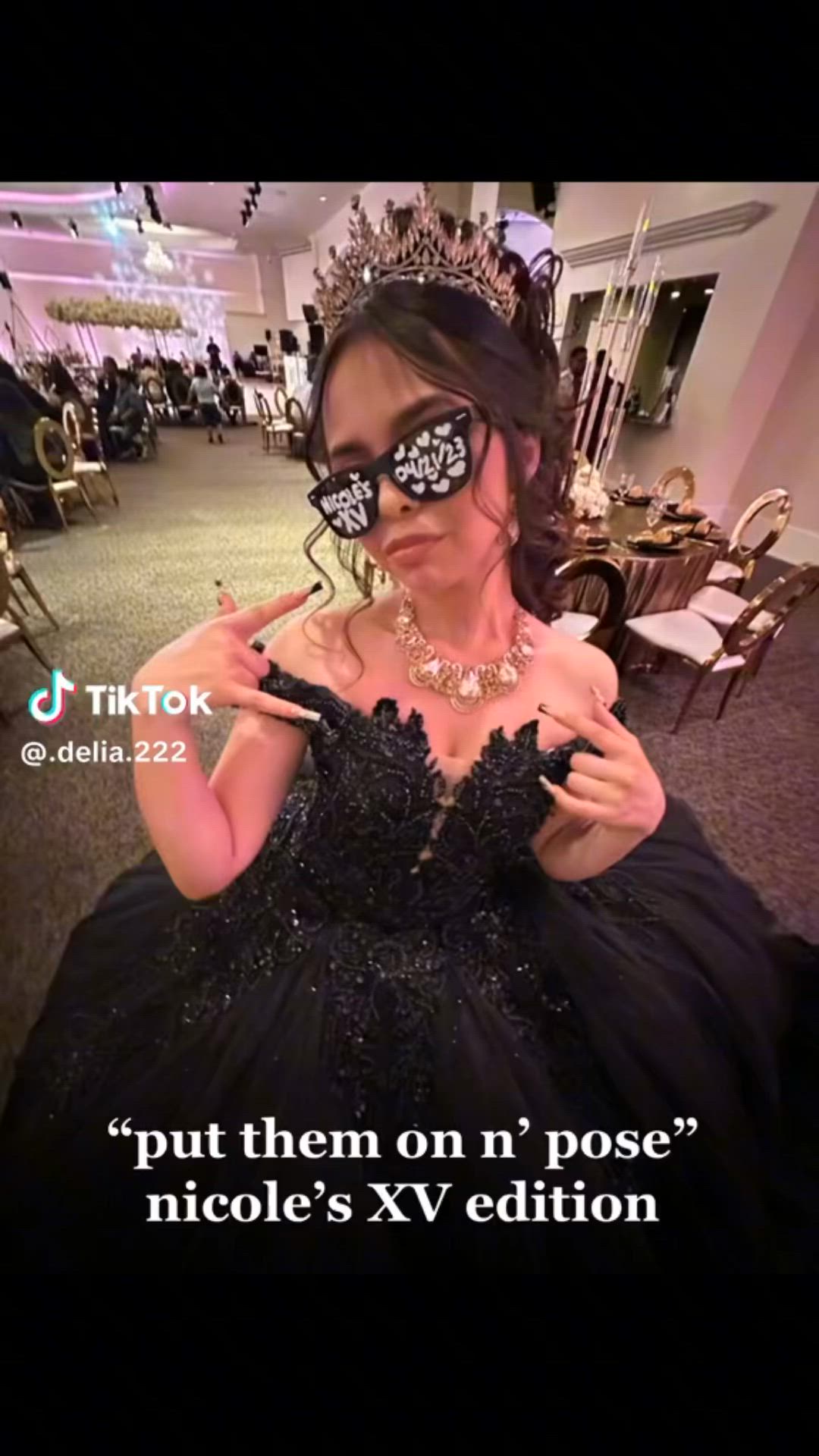 This may contain: a woman in a black dress wearing a mask and holding her hand up to the camera