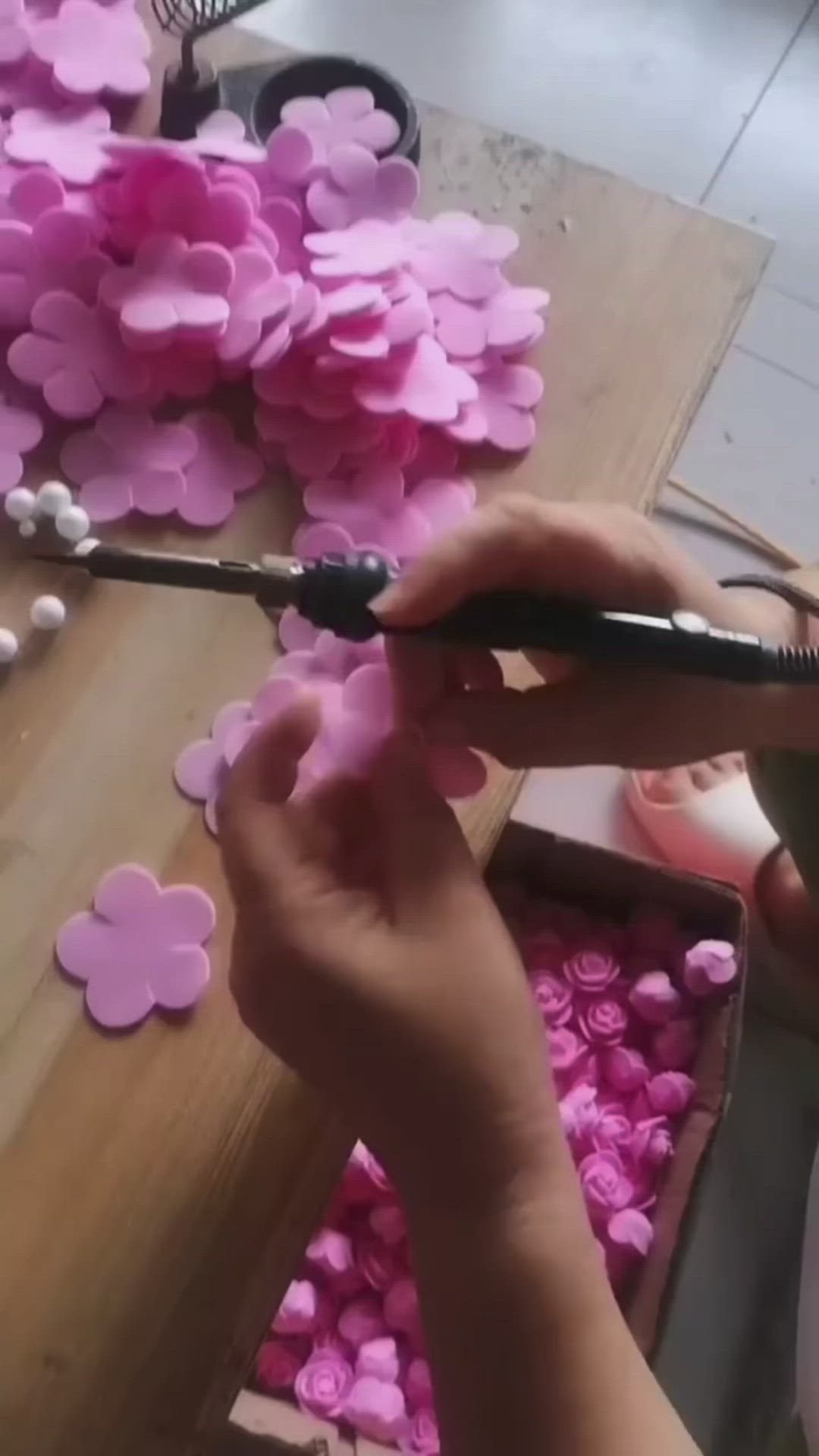 This may contain: a person cutting paper flowers with scissors on a wooden table surrounded by pink and white hearts