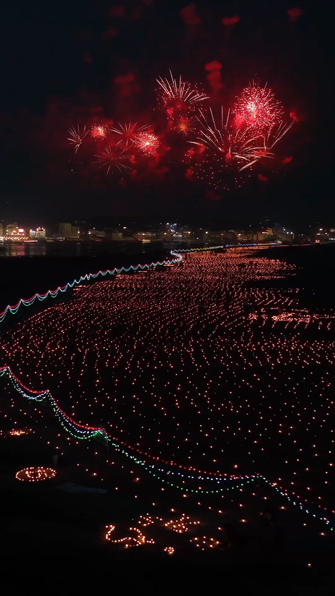 This may contain: fireworks are lit up in the night sky over a beach with lights all around it