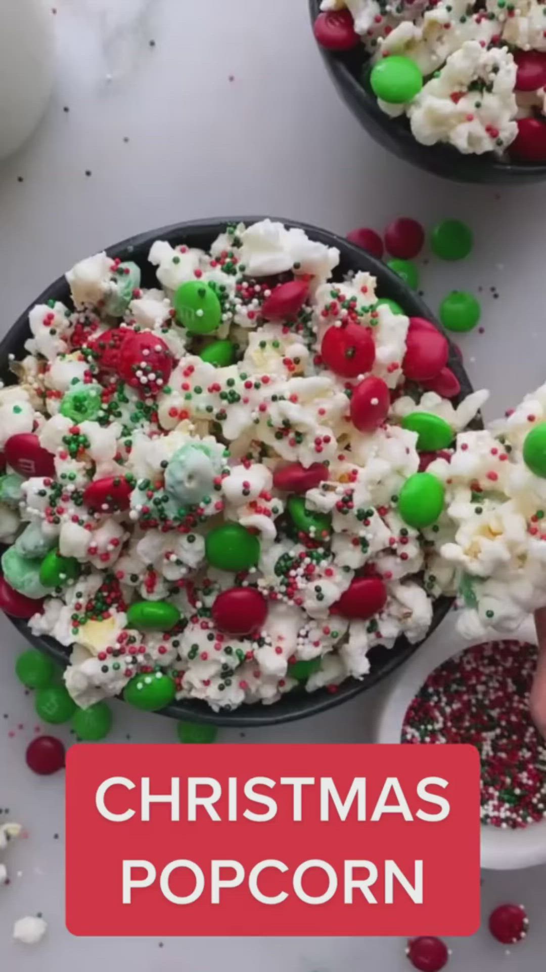 This may contain: christmas popcorn with sprinkles and candy on the side in two black bowls