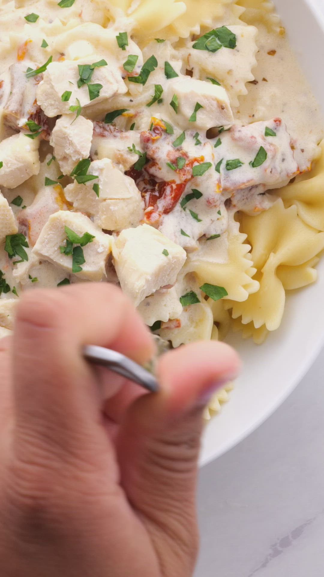 This may contain: a white bowl filled with pasta covered in chicken and cheese sauce next to a fork