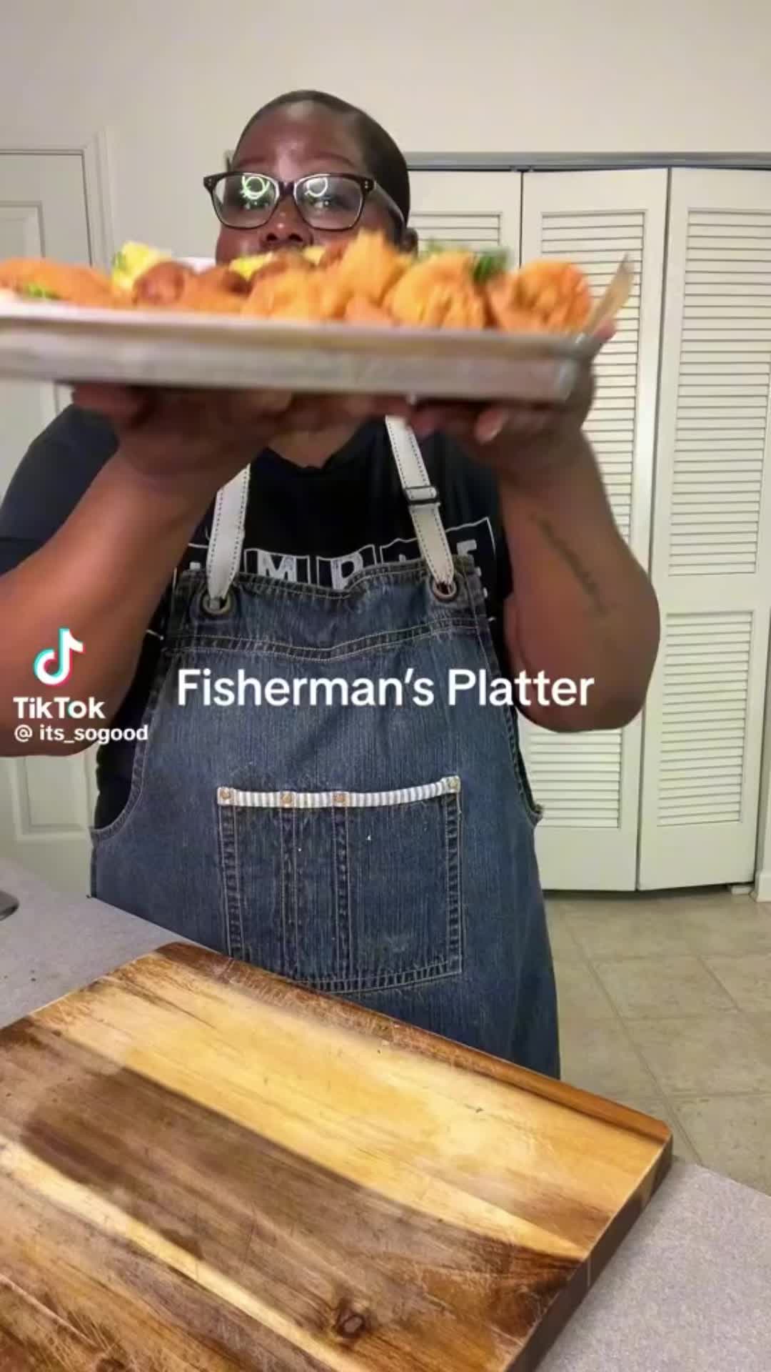 This may contain: a woman in an apron is holding a tray of fried shrimp and breaded potatoes