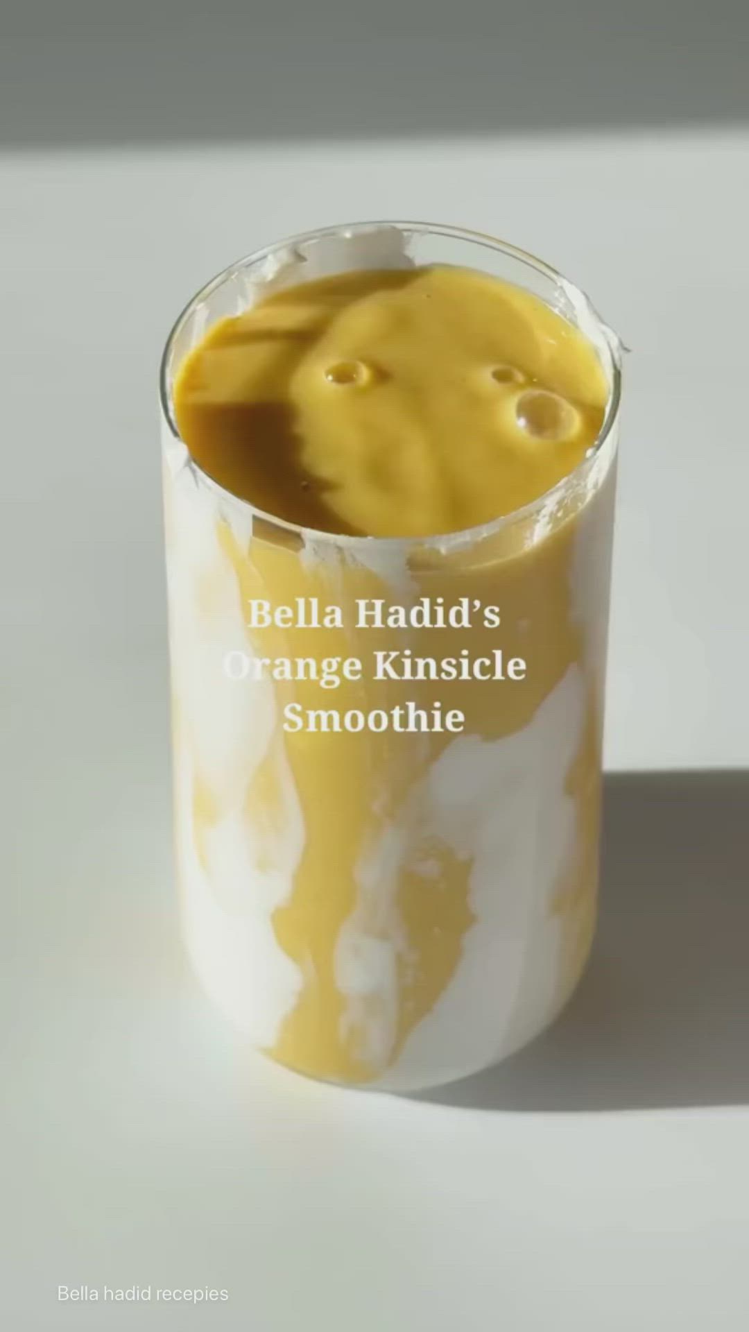 This may contain: a person holding a cup with liquid in it and the words stella haddil's orange kinsicle smoothie