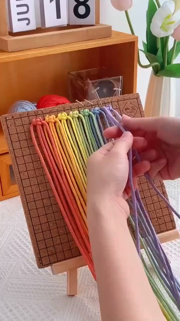 This may contain: a person is knitting yarn on a wooden table with flowers in the background and a shelf full of crochet hooks