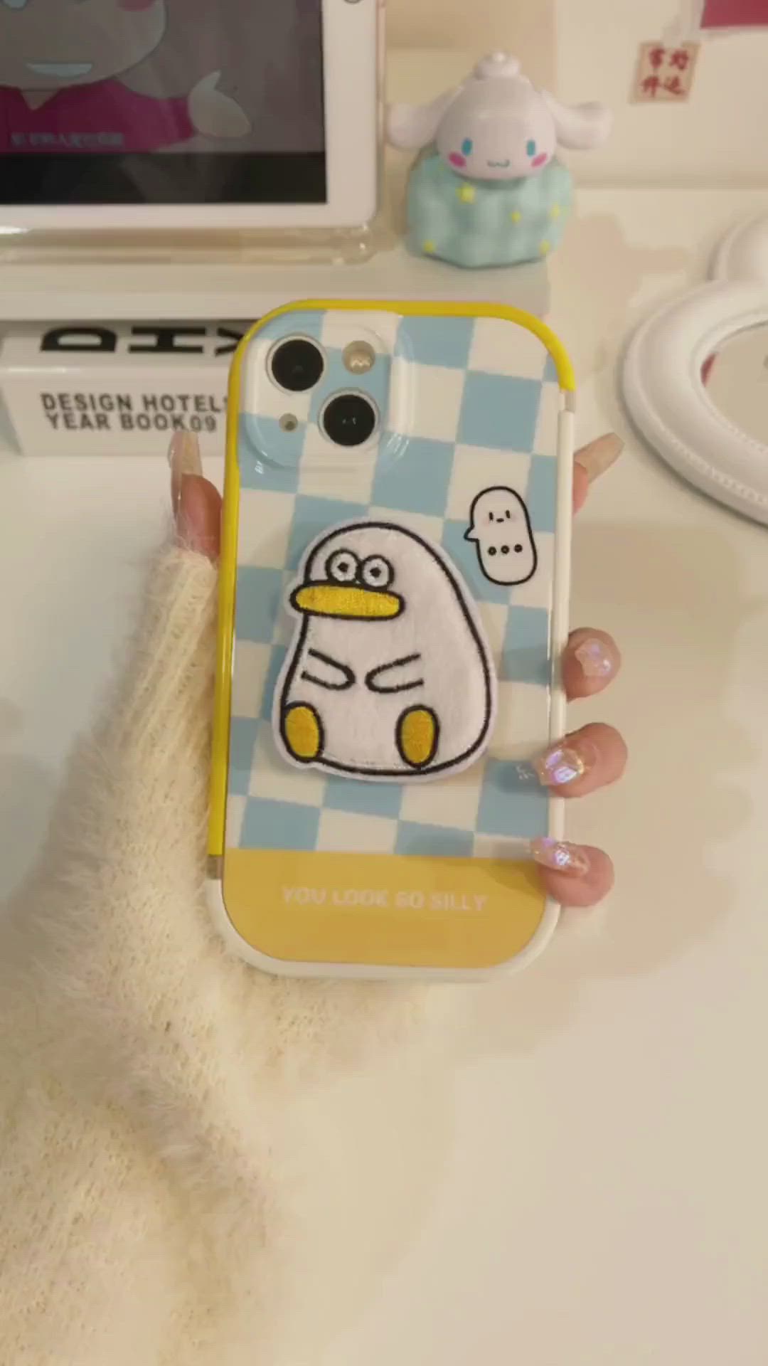 This may contain: a person holding up a cell phone case with a cartoon penguin on the front and side