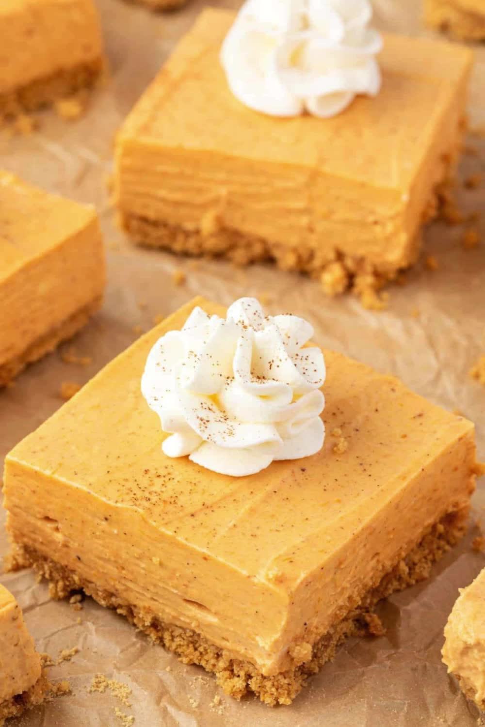 This may contain: no - bake pumpkin cheesecake bars on parchment paper with text overlay that reads, no - bake pumpkin cheesecake bars